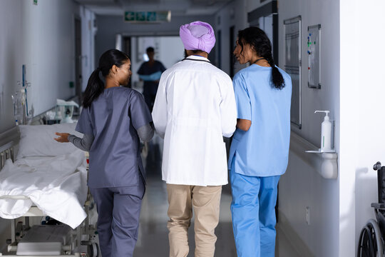 Rear view of diverse doctors discussing work and walking together in corridor at hospital