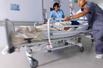 Diverse doctors urgently pushing patient lying in bed in corridor at hospital