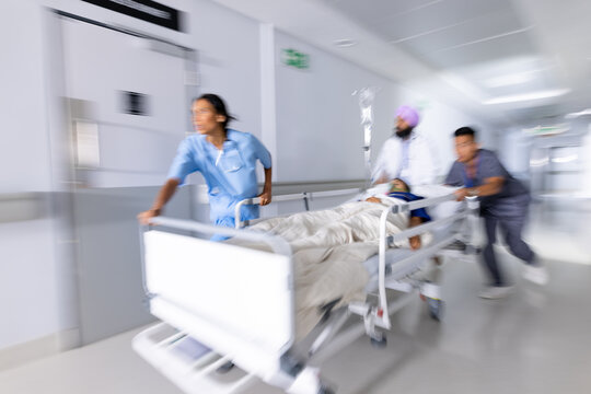 Diverse doctors urgently pushing patient lying in bed in corridor at hospital