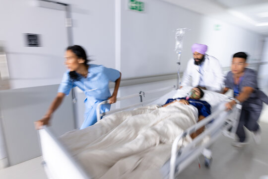 Diverse doctors urgently pushing patient lying in bed in corridor at hospital