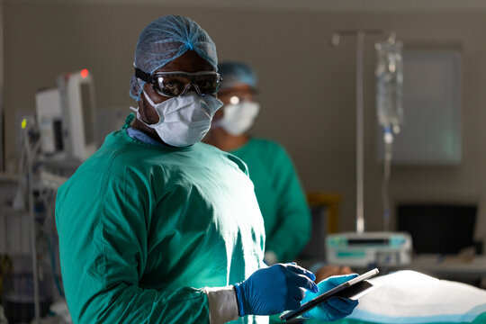 Portrait of african american male surgeon using tablet during surgery in operating theatre