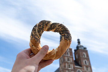 Hand holding obwarzanek krakowski pretzel on Cracow Main Market Square. St. Mary's Basilica,...