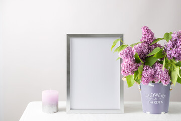 Floral card or poster mockup or silver photo frame in modern style with lilac plant flowers in bucket vase on white table cloth.