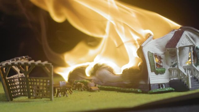 Macro shot of a white model house on fire and miniature lawn furniture melting down