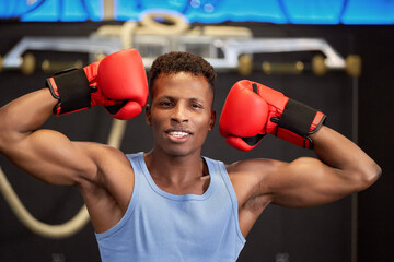 Powerful and Fit African American Boxer Displaying His Strong Muscles and Boxing Gloves in the Gym,...