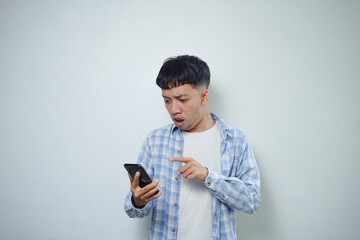 facial expression of astonished asian man using mobile phone holding chin isolated on white background