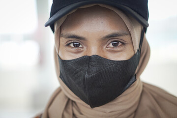 close up of a smiling young woman wearing a hijab wearing a black mask and hat