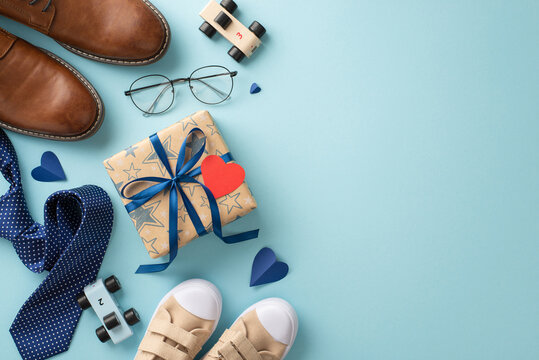 Honor Father's Day with a touching top view image of a tiny son congratulating his dad. Featuring daddy's shoes, little son's sneakers, toys, hearts, tie, spectacles and giftbox, pastel blue backdrop