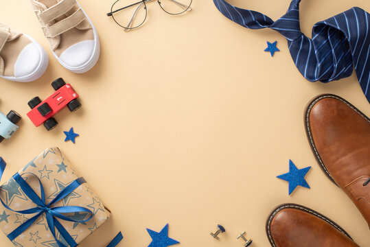 Cute son sends warm wishes to his father on Father's Day. Top view of daddy's shoes, little boy's sneakers, star motifs, toy cars, glasses, tie, giftbox on neutral backdrop with frame for text or ad
