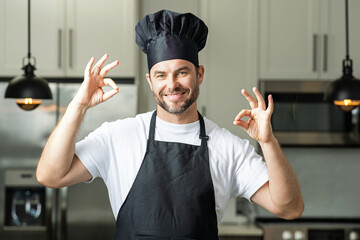 Handsome man chef in uniform cooking in the kitchen. Chef cook with ok sign, delicious food. Male...