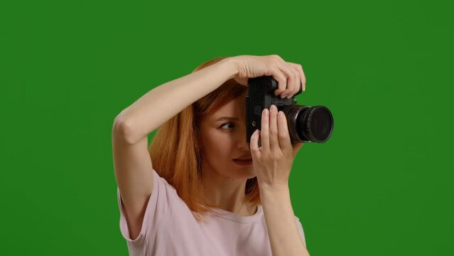 Side view of female photographer taking picture enthusiastically while standing on green screen background. Pleased photographer with the shooting on workplace.