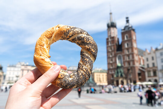 Hand holding obwarzanek krakowski prezel on Cracow Main Market Square. St. Mary's Basilica, Bazylika Mariacka Krak&oacute;w or Kości&oacute;ł Mariacki Church in bg. Krakowskie obwarzanki food in Krakow, Poland.