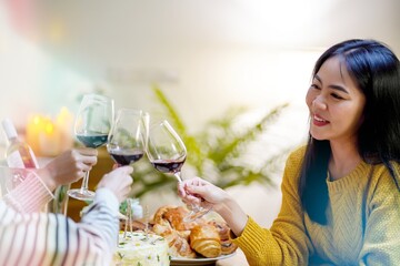 Cheerful friends enjoying home Birthday holiday party. Asian Friends cheering drinking red wine celebrating Christmas or New Year party