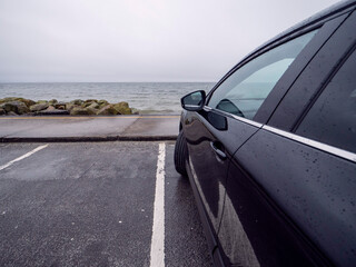Fototapeta na wymiar Side of a dark color car parked in parking lot by the ocean. Travel to nature concept.
