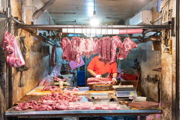 Salesman butchering pork on white chopping board in local market, chef butchering pork on table. Pork parts hanging in a pork shop at Fresh Market. - 603933300