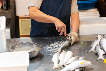 Merchants fillet fish on a white chopping board in a traditional market, chefs fillet fish at a table.
