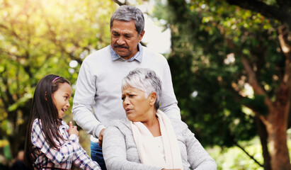 Grandparents, park and old woman in wheelchair together with her husband and granddaughter. Person with a disability, family or kids and girl child bonding with her senior relatives in natural garden