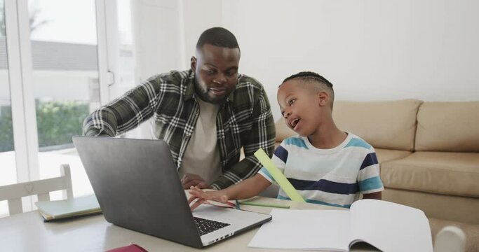 Happy african american father and son using laptop, in slow motion