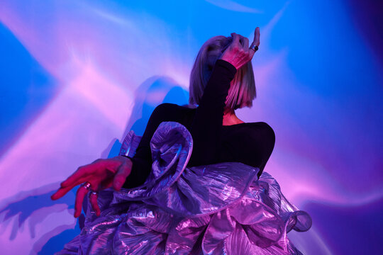 Horizontal medium studio shot of unrecognizable senior Caucasian woman with blond hair wearing unusual outfit posing on camera in neon light 