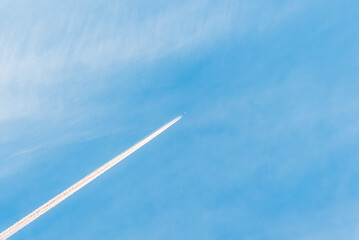An airplane and a white trail from an airplane in a blue summer sky.airplane flying through blue...