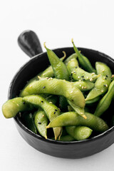 japanese edamame beans snack in black ceramic bowl on white background