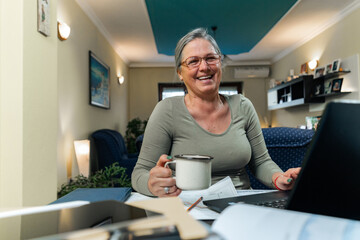 Smiling senior woman with white beard using laptop drinking a coffee.