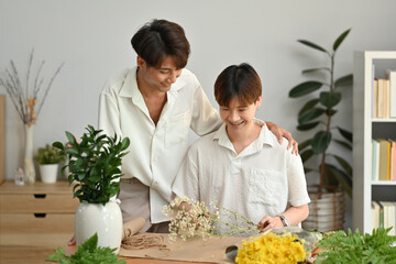 Cheerful gay couple arranging flowers, spending good time together at home. LGBT, love and...