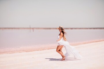 Fototapeta na wymiar Woman in pink salt lake. She in a white dress and hat enjoys the scenic view of a pink salt lake as she walks along the white, salty shore, creating a lasting memory.