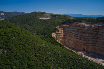 Extraction of marble in a mountain quarry. Steps of a marble quarry in the background green forest blue sky. Plot of marble quarry against the blue sky.