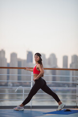 Sporty Healthy Lifestyle Concept. Beautiful woman with long black hair doing legs stretching exercises, morning aerobic classes with beautiful panoramic view of city, film grain effect, soft focus