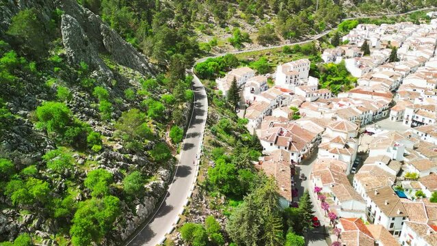 Panning drone clip of edge of Grazalema national park, showing a forested mountainside with windy tarmac road, and traditional spanish buildings