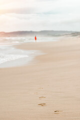 Obraz premium Beach travel - woman in a red dress walking along the beach leaves footprints in the sand.