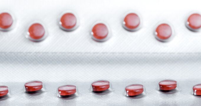 Red colored pills arranged in a raw. Focus line in the foreground. Pharmaceutical package manufacturing.