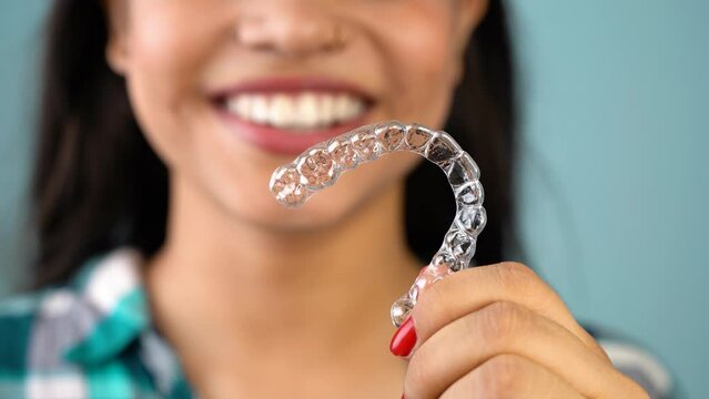 Young Asian Indian woman holding removable invisible aligner, also known as invisalign or  clear aligner