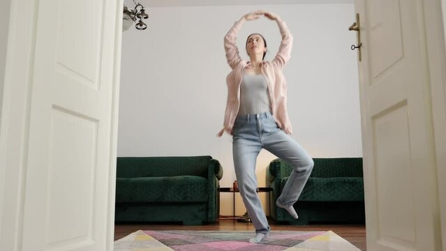 Young Caucasian woman wearing casual clothes learning to dance ballet in home. Low angle view through door. Concept of dance training