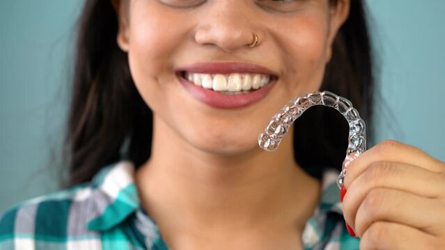 Young Asian Indian woman holding removable invisible aligner, also known as invisalign or  clear aligner
