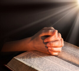 Hands clasped in prayer near an open book