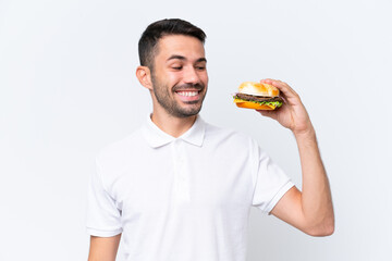 Young handsome caucasian man holding a burger over isolated background with happy expression