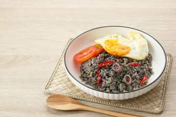 Nasi Goreng Cumi Hitam or Black Squid Fried Rice, served in white plate on wooden table
