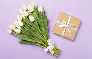 White tulip bouquet with gift on color background, top view