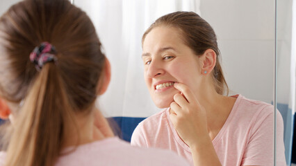 Portrait of smiling young woman opens mouth and looks at the reflection of her teeth in mirror. Concept of teeth health, self checking mouth and oral hygiene.