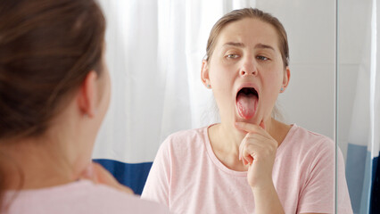 Portrait of young brunette woman checking her tongue for plaque and microbes while looking in mirror