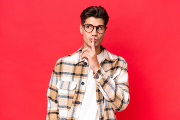 Fototapeta premium Young caucasian handsome man isolated on red background showing a sign of silence gesture putting finger in mouth