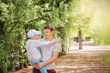 Photo portrait of a happy young dad and his son. Dad holds his son in his arms, playing in the park on a sunny summer day.