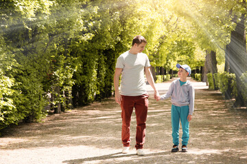 Photo portrait of a happy young dad and his son, walking hand in hand through the park and smiling, sunny summer day.