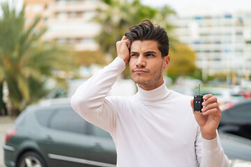 Young caucasian man holding car keys at outdoors having doubts and with confuse face expression