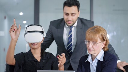 Young woman testing VR glasses or goggles working with two colleagues. Business team of three people working on virtual reality in meeting room at modern office. Meeting with technology