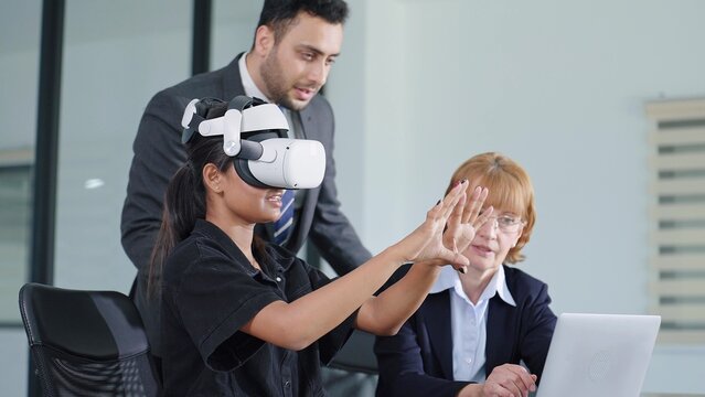 Young woman testing VR glasses or goggles working with two colleagues. Business team of three people working on virtual reality in meeting room at modern office. Meeting with technology - Powered by Adobe