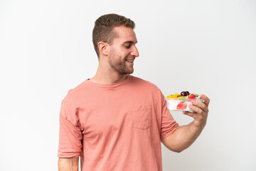 Young caucasian man holding a bowl of fruit isolated on white background with happy expression