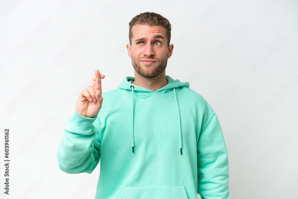 Wall mural Young handsome caucasian man isolated on white background with fingers crossing and wishing the best